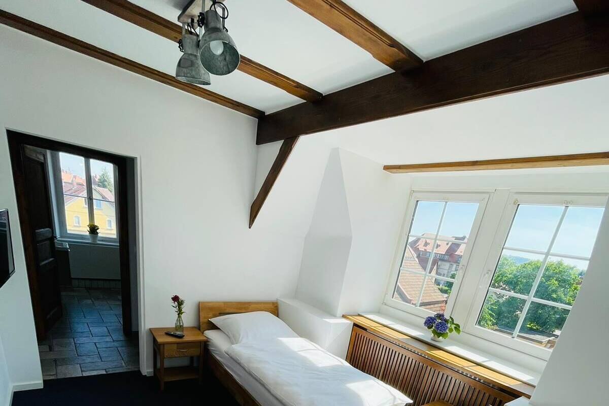 Un dormitorio con dos camas, cabecero de madera, mesita de noche con lámpara, ventana con vistas y radiador.