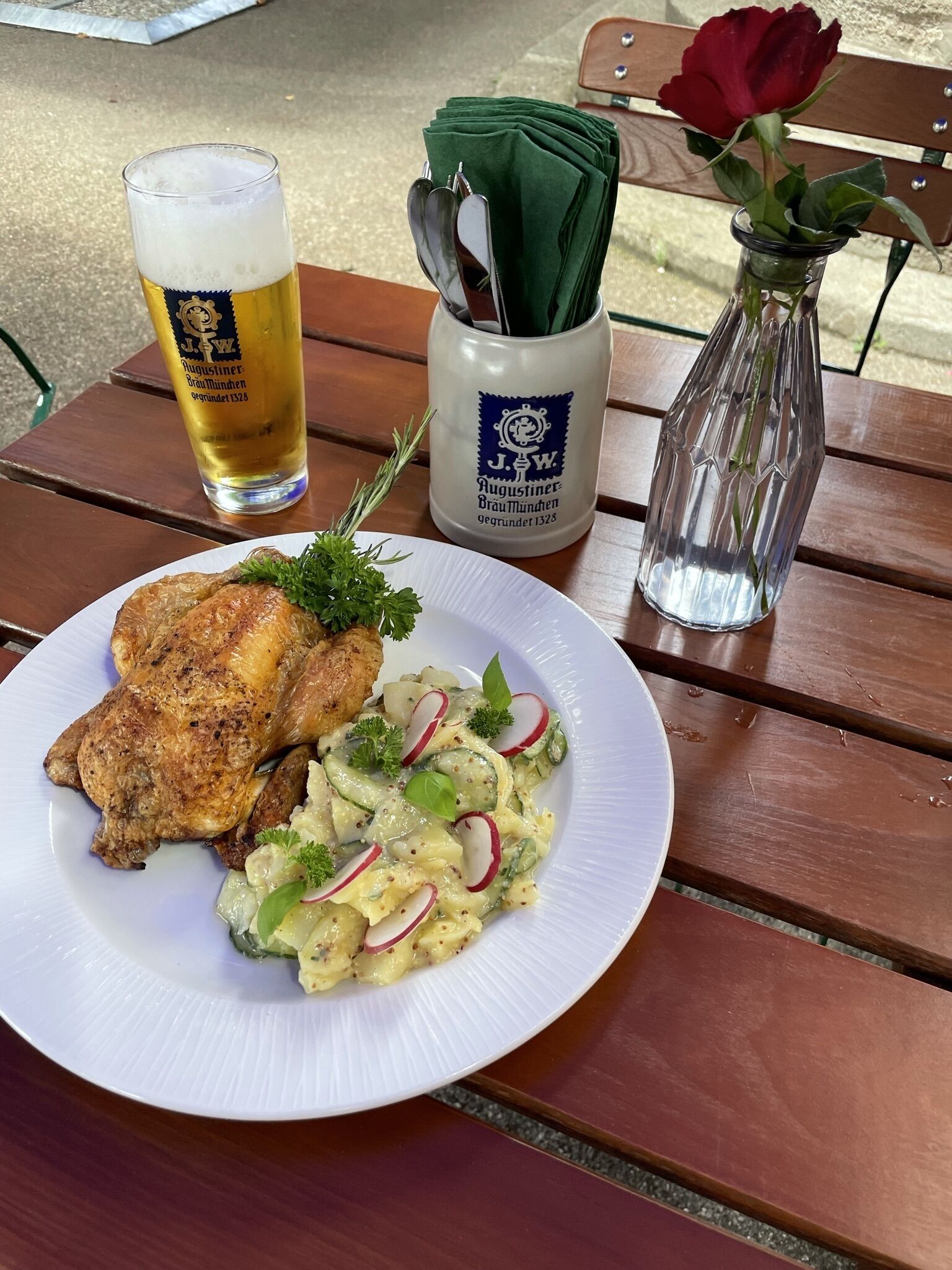 A plate with a piece of meat and a salad, a glass of beer, and a vase with a rose on a wooden table.