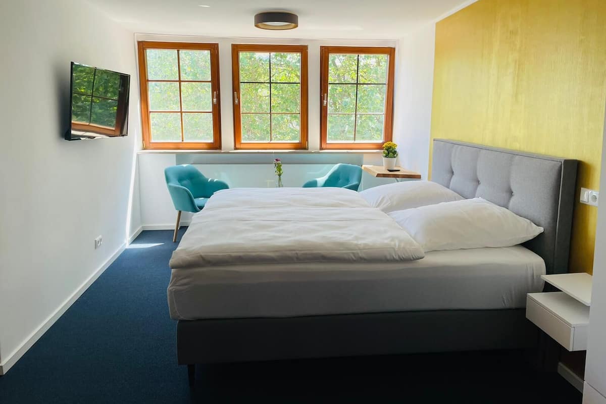Un dormitorio con cama, escritorio, silla y tres ventanas.
