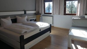 Une chambre moderne avec un grand lit, deux fenêtres avec des rideaux, un radiateur et une petite table.