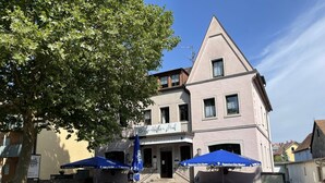 Un hôtel avec une enseigne indiquant « Bayerischer Hof » et des tables à l’extérieur, protégées par des parasols bleus.