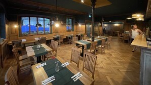 Un restaurant doté de meubles en bois, de grandes fenêtres et d’un espace bar.