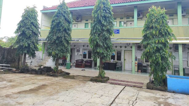 A building with a tiled roof, green pillars, and multiple windows. There are potted plants in front of the building. - OYO 90333 Wisma Tenang Jaya Syariah (Jatiwangi)