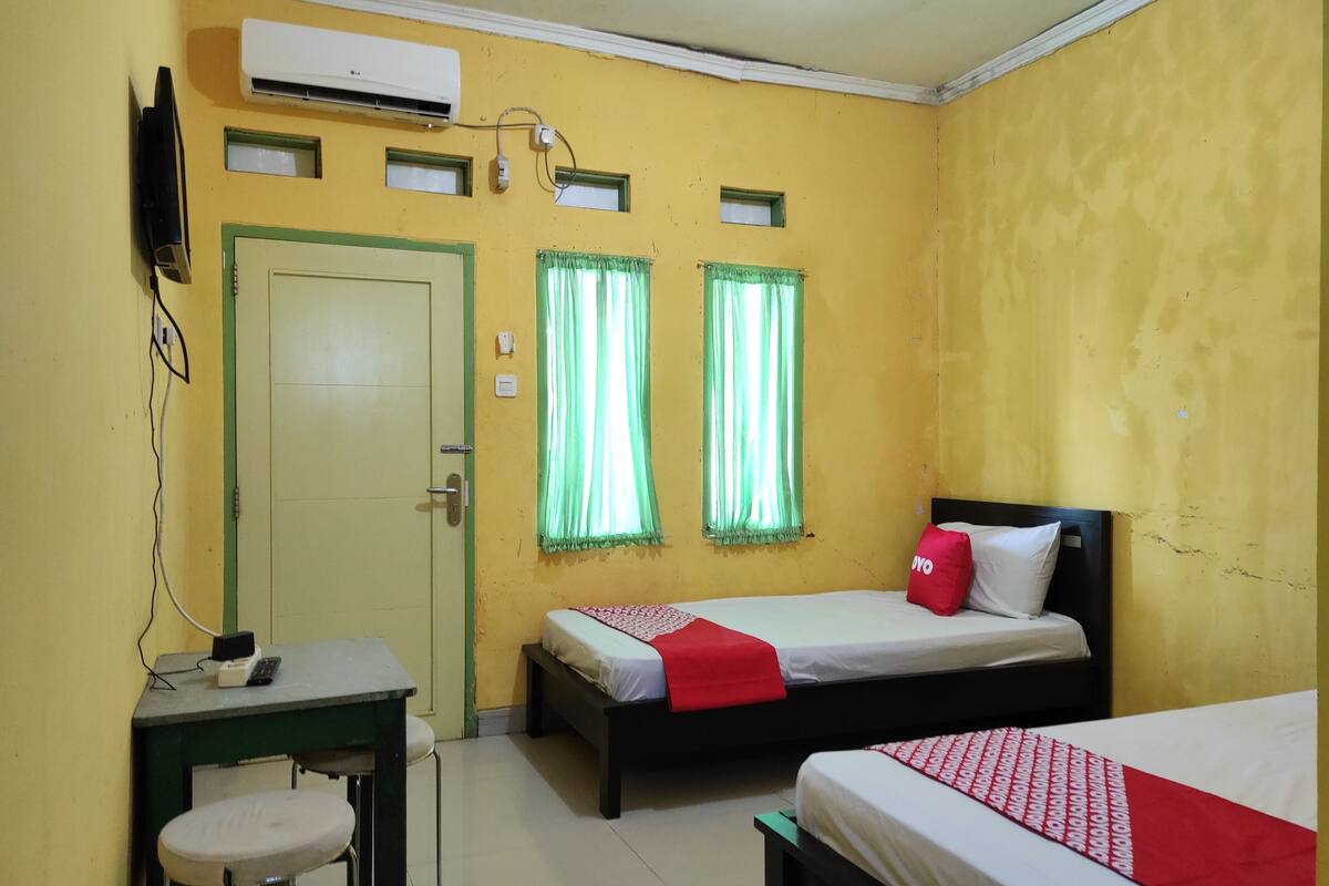 A room with two beds, a desk, and an air conditioning unit on the wall.