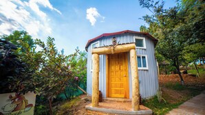 Una pequeña cabaña de madera con puerta de madera y techo rojo, rodeada de follaje.