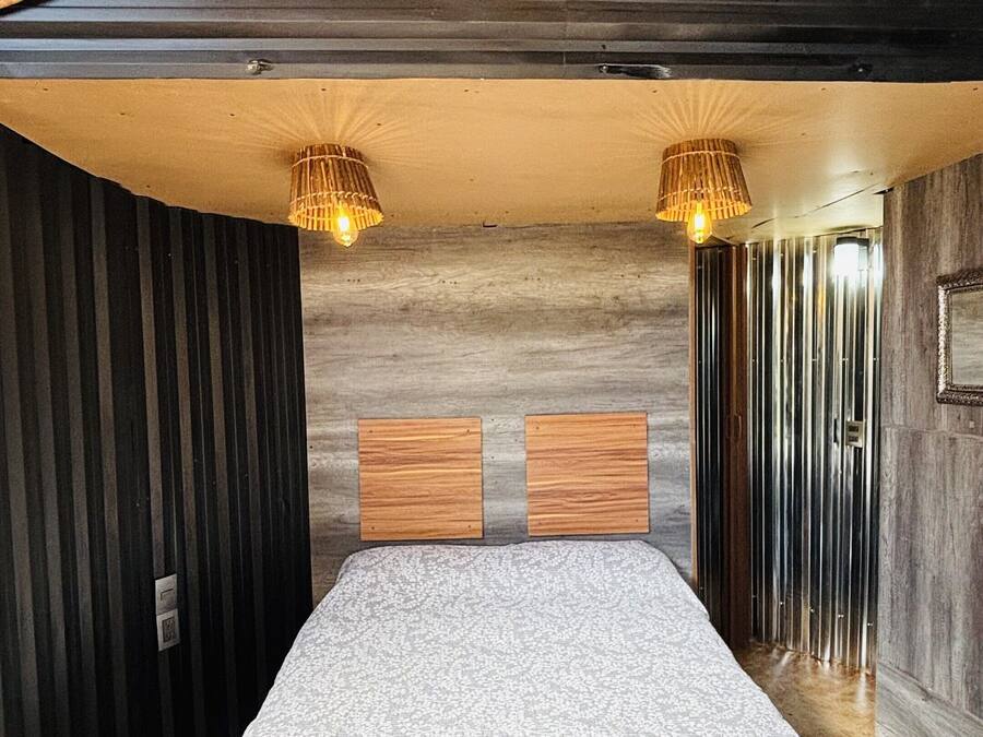 Une chambre dotée d’un grand lit, d’une tête de lit en bois, de deux lampes fixées au mur et d’un plafond orné de motifs en forme d’étoiles.