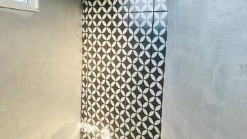 Un baño con pared de azulejos de diseño geométrico, una ventana y zona de ducha.