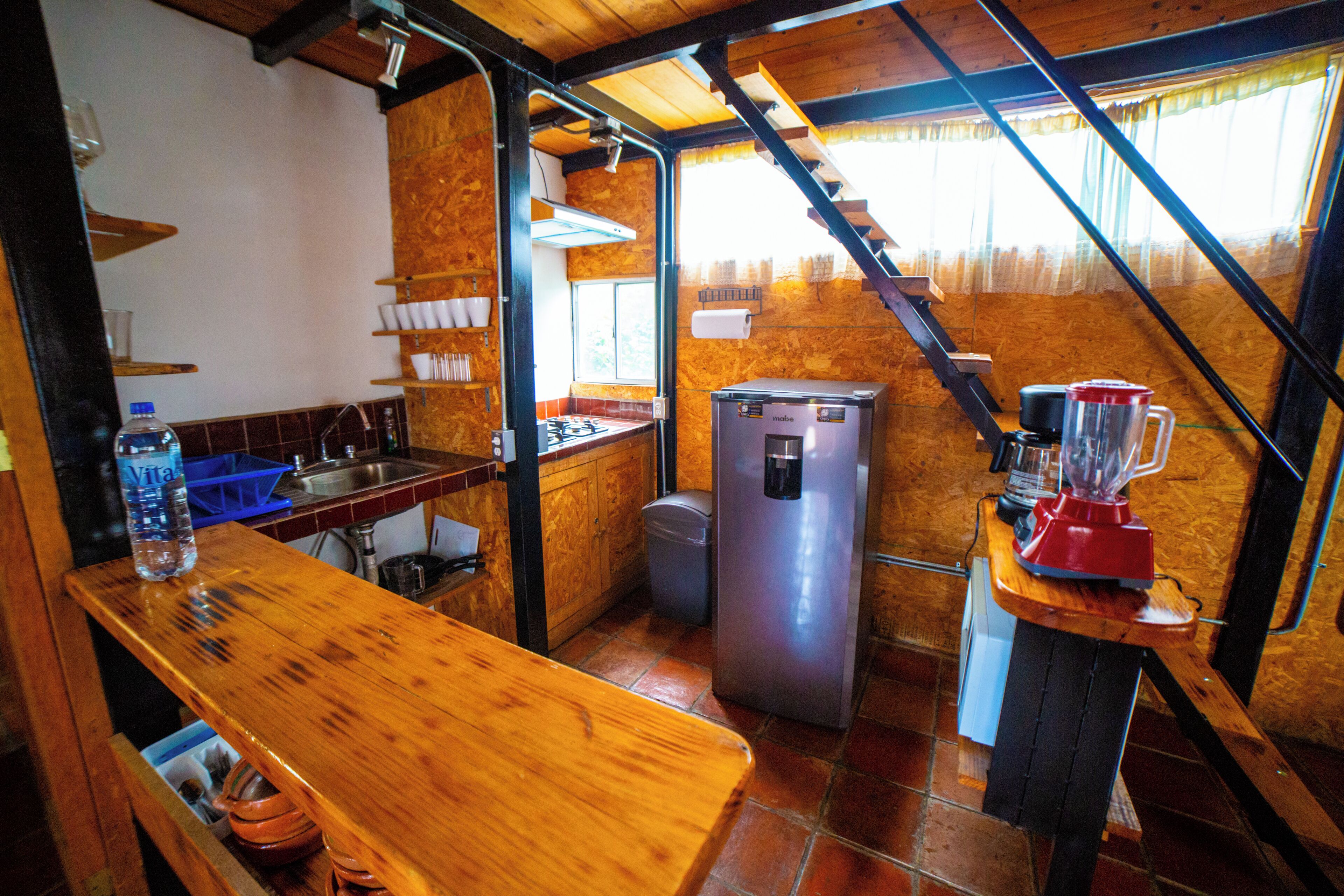 A compact kitchen with a wooden counter, a refrigerator, a blender, and a sink.