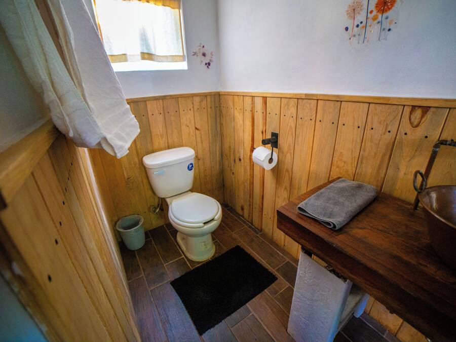 A small, wooden-paneled bathroom with a toilet, sink, and a window.