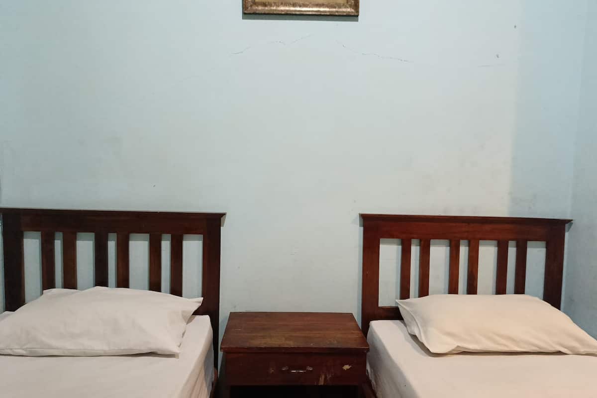 A room with two wooden beds, each with a white mattress and pillow, and a small wooden nightstand between them.