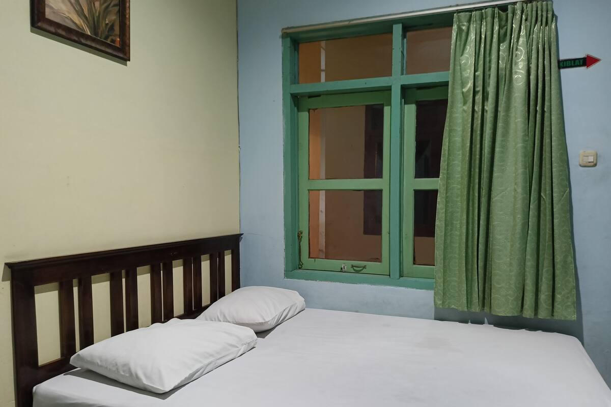 A single bed with white bedding in a room with a green window and curtains.