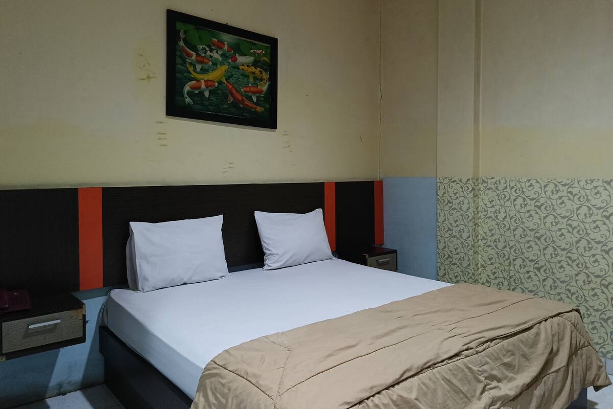 A bedroom with a bed, white pillows, a headboard with red and black stripes, a nightstand, and a painting of fish on the wall.