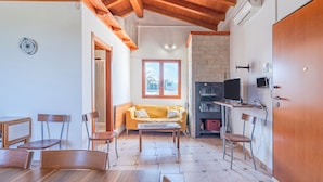 Une pièce avec un plafond en bois, un canapé, une table à manger avec des chaises, un téléviseur et une cheminée.