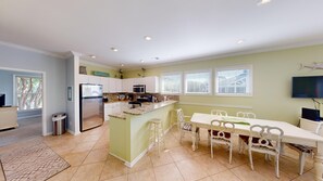 Una cocina moderna con una isla central, armarios blancos y una zona de comedor con mesa y sillas blancas.