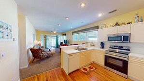 A compact kitchen with white cabinets, a microwave, a stove, and a sink. There is a dining area with a table and chairs, and a ceiling fan. - Beautiful 2BR 2BA Lakeside Villa with Lake Views (Pawleys Island)