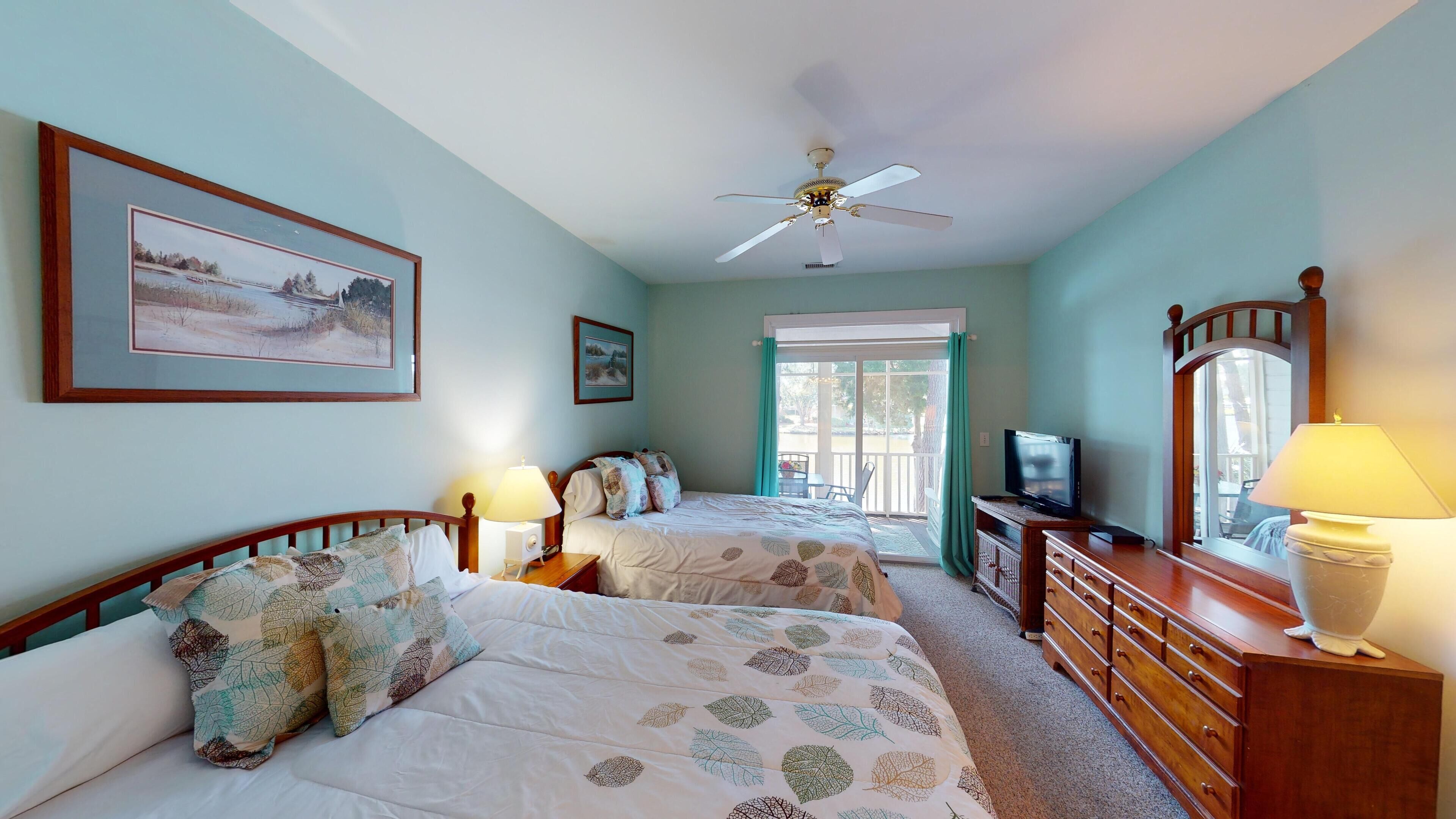A bedroom with two beds, a ceiling fan, a television, and a dresser.