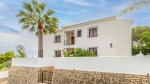 A two-story building with a stone wall, a palm tree, and a clear sky. - Villa 'La Boniquesa Bajo' with Sea View, Wi-Fi and Air Conditioning (Benissa)