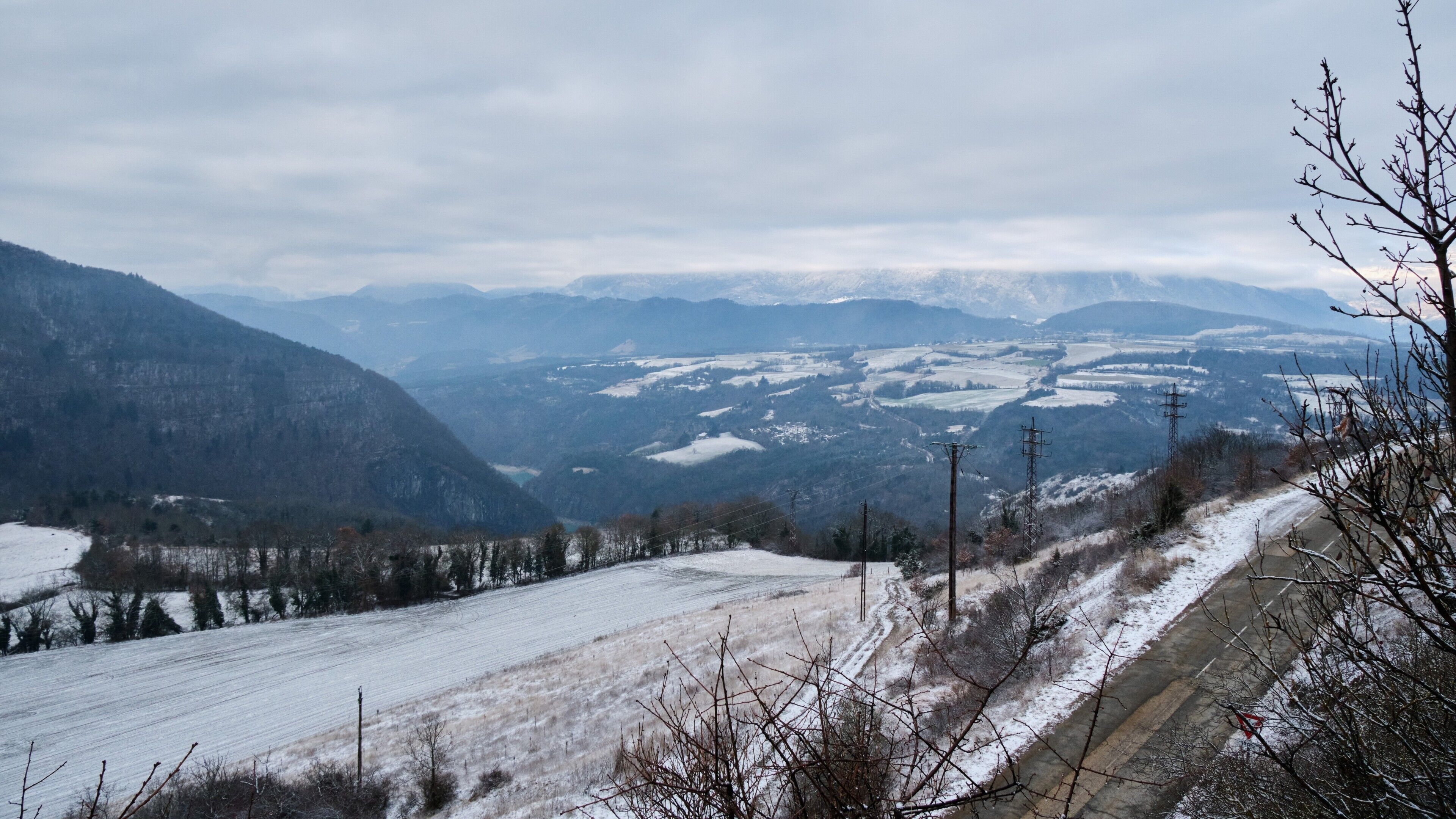 Een besneeerd landschap met bergen, een weg en elektriciteitskabels.