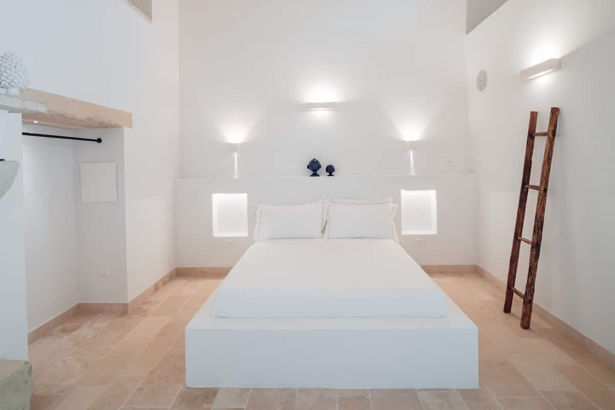 Un dormitorio minimalista con una cama grande, dos lámparas fijadas a la pared y una escalera de madera.