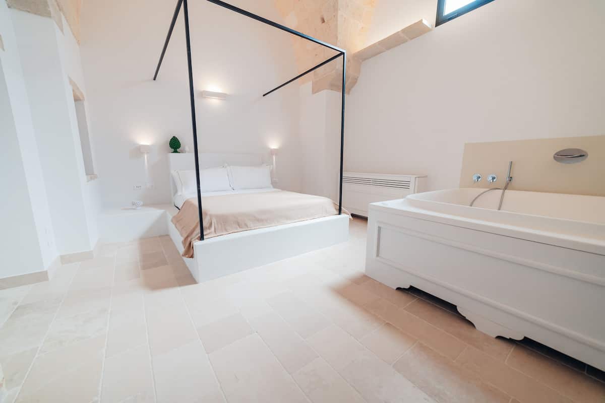 Un dormitorio moderno con una cama con dosel, una bañera grande y una mesita de noche pequeña.