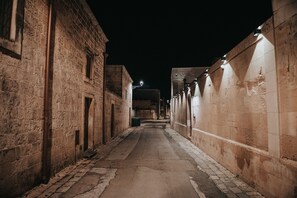 Un estrecho callejón flanqueado por edificios de piedra, un sendero empedrado y un farol a lo lejos.