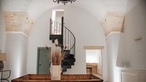Ein geräumiges Zimmer mit einem Holztisch, einer Vase mit Trockenpflanzen, einer schwarzen Wendeltreppe und einer hellblauen Tür.