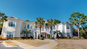 A large, two-story house with a central entrance, surrounded by palm trees and a well-maintained lawn. - Escape to Green Haven a Golfer's Delight (Pawleys Island)