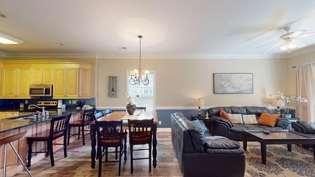 A spacious living area with a dining table, chairs, a sofa, and a coffee table. There is a kitchen area with yellow cabinets and a microwave. - Escape to Green Haven a Golfer's Delight (Pawleys Island)