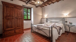 Un dormitorio con cama, armario de madera, ventana y una mesita con un florero.