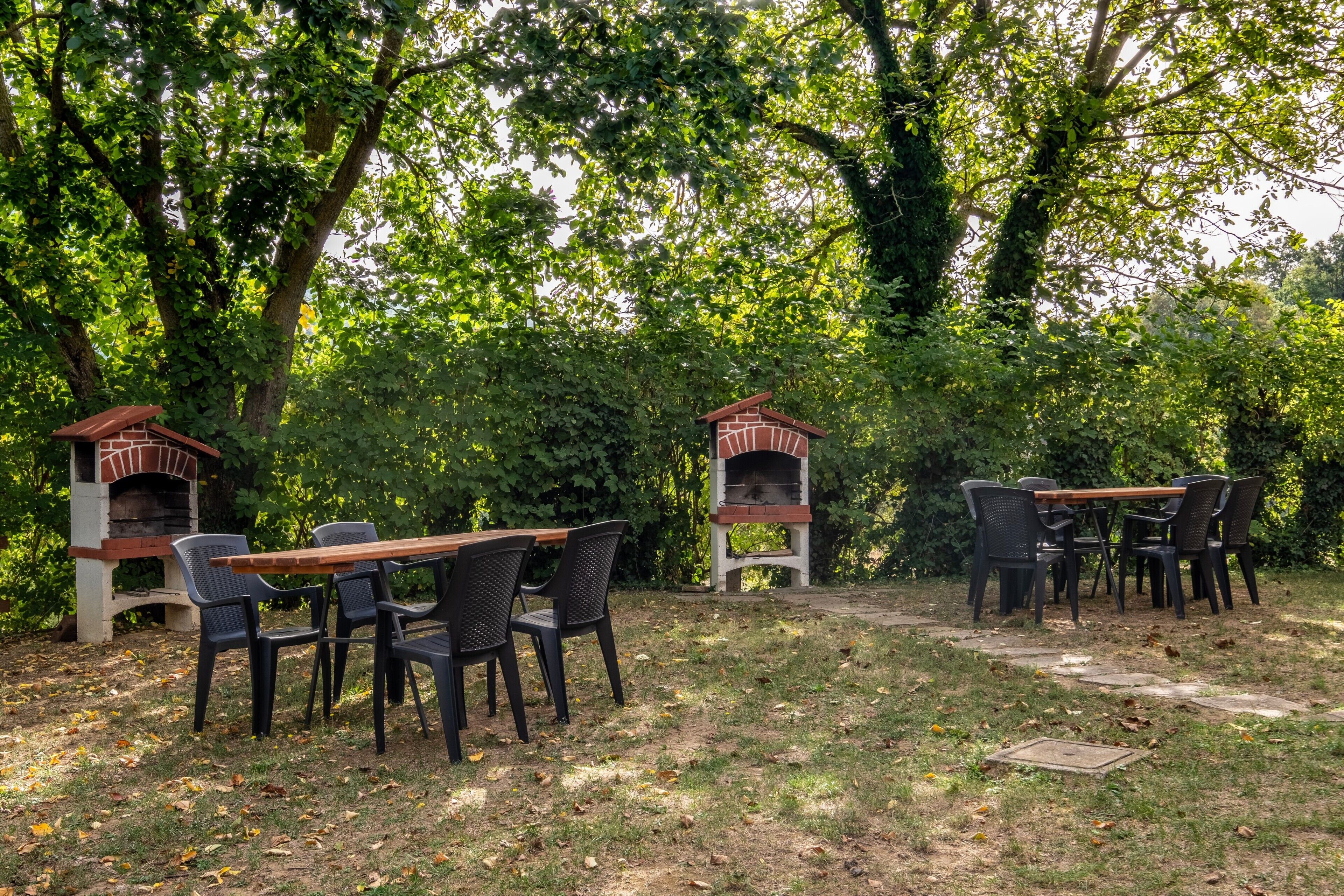 An outdoor patio with two brick pizza ovens, a wooden table, and black chairs.
