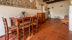 A dining area with a wooden table and chairs, a stone wall, and a tiled floor. - "Ginestra" Apartment in Farmhouse with Shared Pool, Mountain View, and Wi-Fi (Arcidosso)