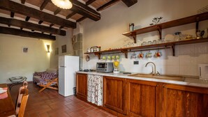 A kitchen with wooden cabinets, a refrigerator, a stove, and a dining area with a table and chairs. - "Ginestra" Apartment in Farmhouse with Shared Pool, Mountain View, and Wi-Fi (Arcidosso)