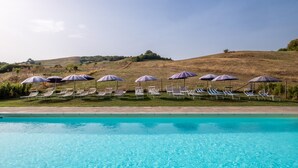 A swimming pool with clear blue water, surrounded by lounge chairs and umbrellas. - "Ginestra" Apartment in Farmhouse with Shared Pool, Mountain View, and Wi-Fi (Arcidosso)