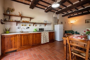 Una cocina con armarios de madera, salpicadero de azulejos, un colgador para ollas y una zona de comedor con mesa y sillas.