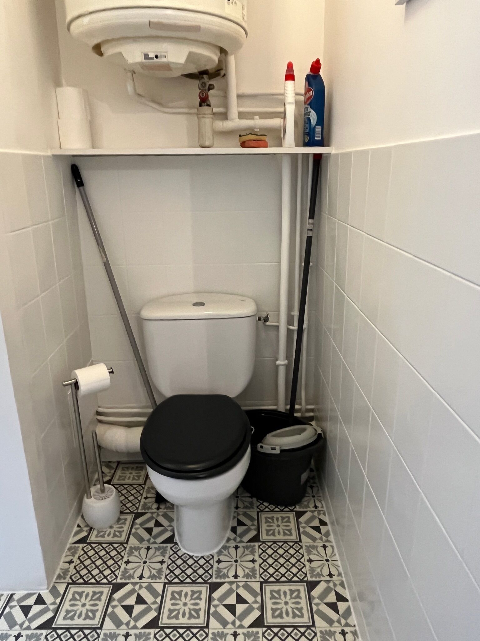 A small bathroom with a toilet, a bidet, a toilet paper holder, and a mop.