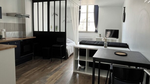 A compact studio apartment with a kitchenette, a dining area, a bed, and a window with curtains.