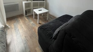A modern room with a black sofa, a TV on a white stand, a small white table, and a window with curtains.