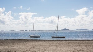 Une plage où deux voiliers sont amarrés dans des eaux calmes, sous un ciel dégagé, avec des montagnes qui se dessinent à l’horizon.