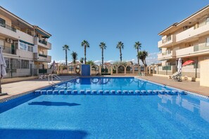 A swimming pool with a tiled edge, surrounded by buildings with balconies and palm trees.