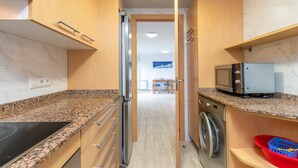 Una cocina con encimeras de granito, armarios de madera, microondas, lavadora y cesto de ropa.