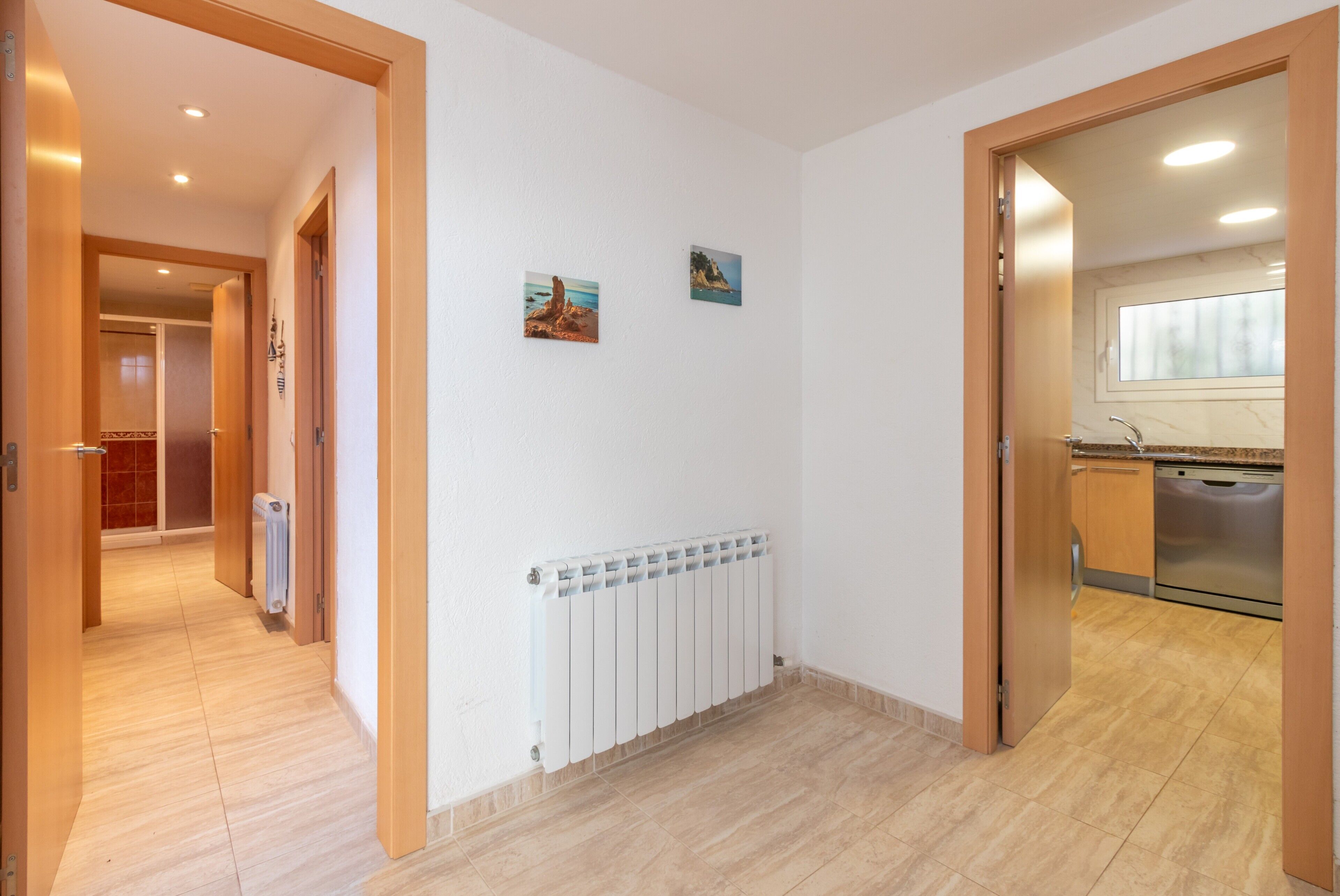 A hallway with a radiator, wooden doors, and a kitchen area with a dishwasher.