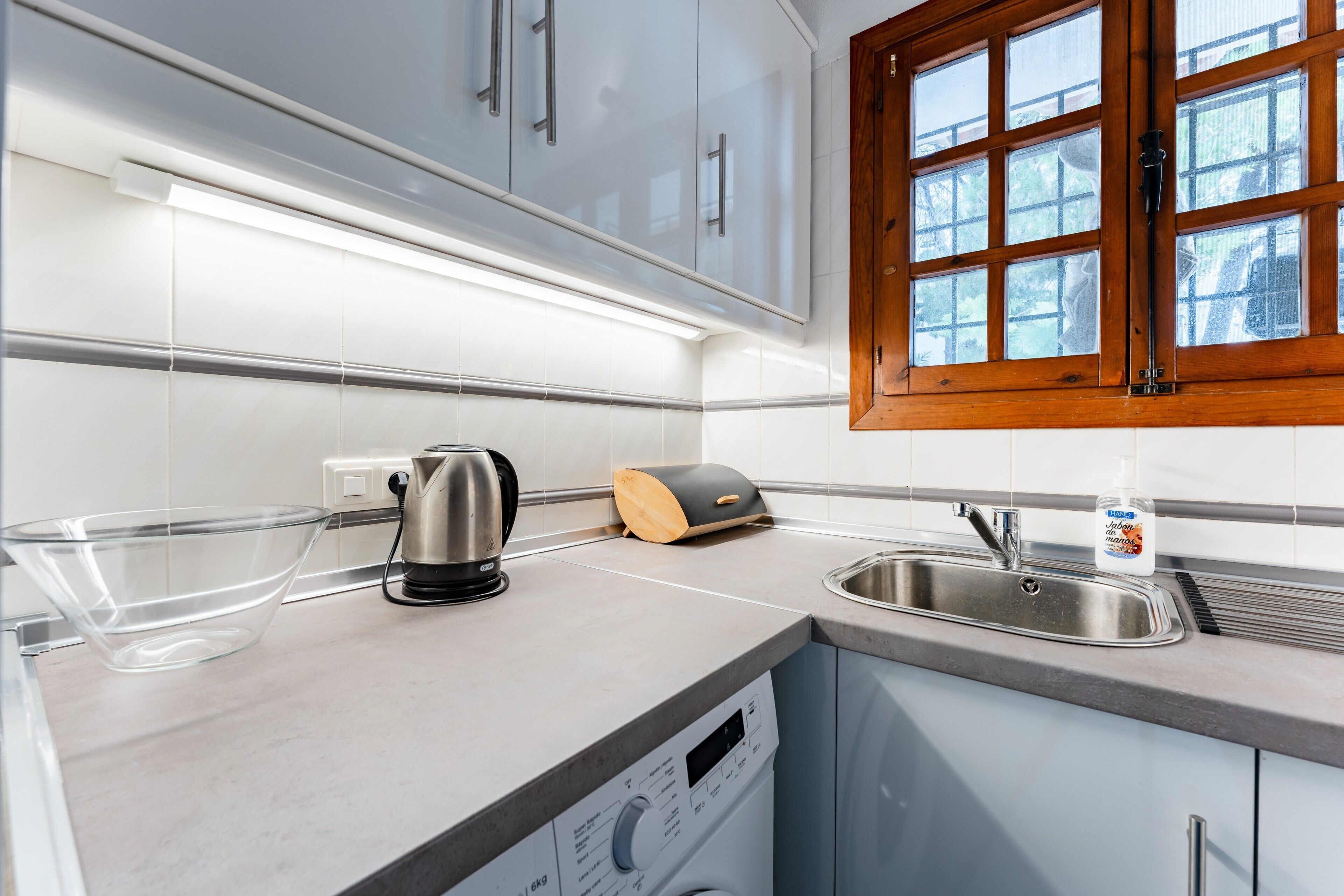A modern kitchen with a built-in dishwasher, a kettle, and a wooden bread box.