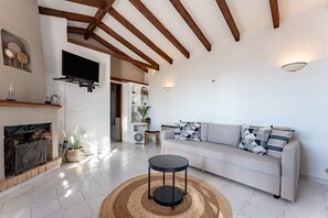 Uma sala de estar com lareira, um sofá, uma mesa redonda e uma televisão fixada na parede.