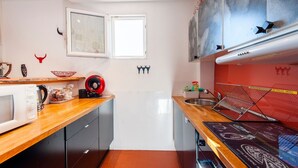 Uma cozinha compacta com micro-ondas, chaleira e um eletrodoméstico vermelho na bancada.