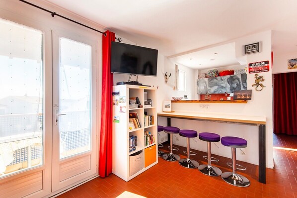 Une pièce dotée d’une porte coulissante, d’un téléviseur, d’une bibliothèque, d’un coin bar avec des tabourets et d’un rideau rouge.