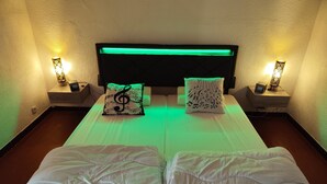 Uma cama de casal com cabeceira, duas mesas de cabeceira com luminárias e almofadas decorativas.