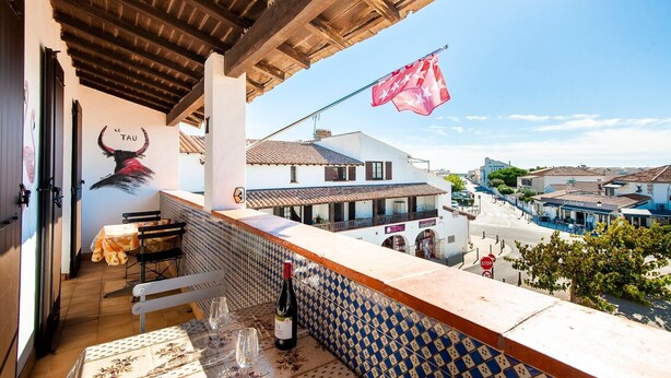 Uma varanda com vista para uma cidade, uma mesa com copos de vinho e uma bandeira.