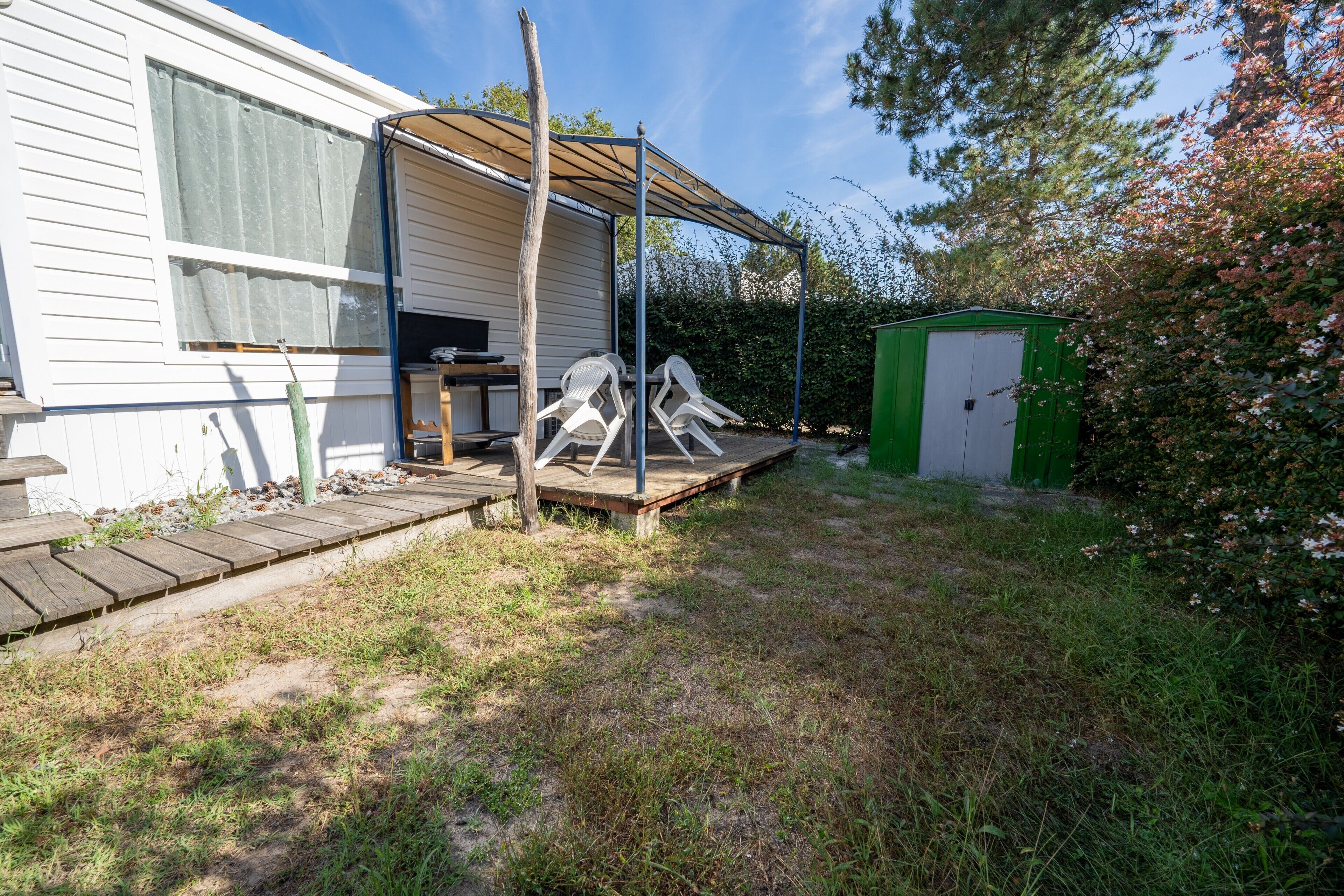 Une maison avec un porche couvert, un abri de jardin vert et une terrasse en bois.