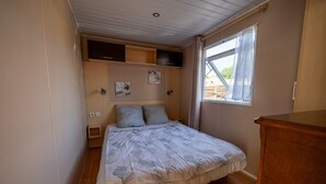 Une chambre à coucher comprenant un lit, une tête de lit en bois, des étagères murales, une fenêtre avec des rideaux et une commode en bois.