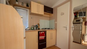 Une cuisine compacte équipée d’une cuisinière, d’un four et d’un four à micro-ondes. Elle comprend une fenêtre avec des stores, un évier et un plan de travail sur lequel se trouvent divers objets.